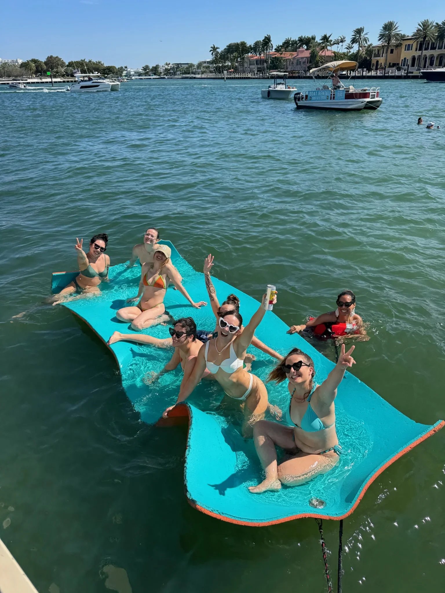 Group of bachelorettes on the Freaky Tiki in a marina, with boats and waterfront houses in the background.