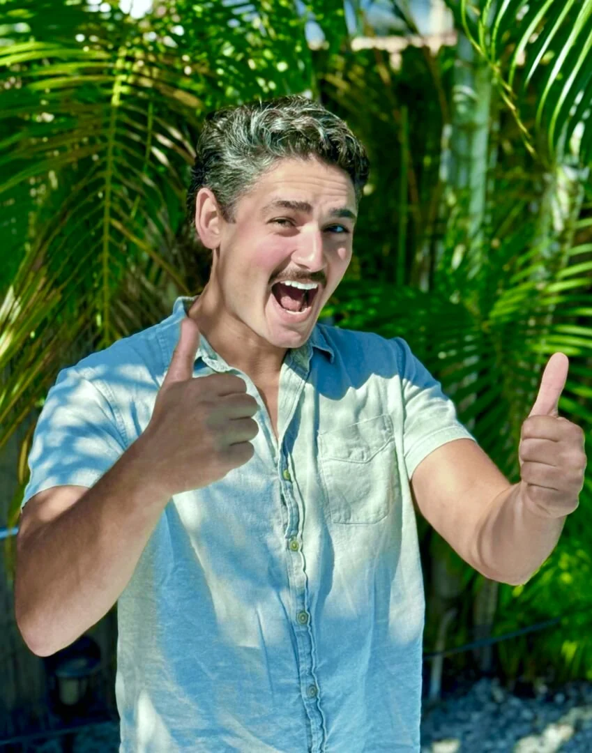 Azeem Sultan, founder of Freaky Tiki Boat Charters, smiling with two thumbs up in front of palms