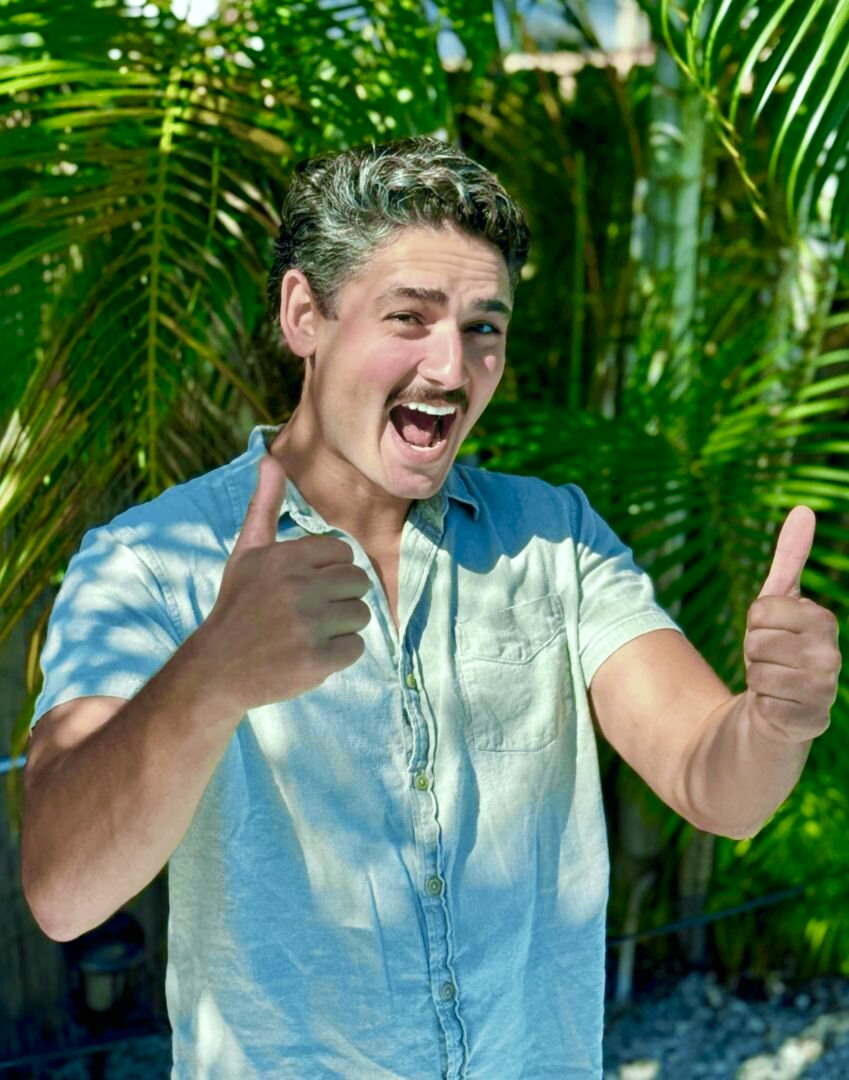 Azeem Sultan, founder of Freaky Tiki Boat Charters, smiling with two thumbs up in front of palms