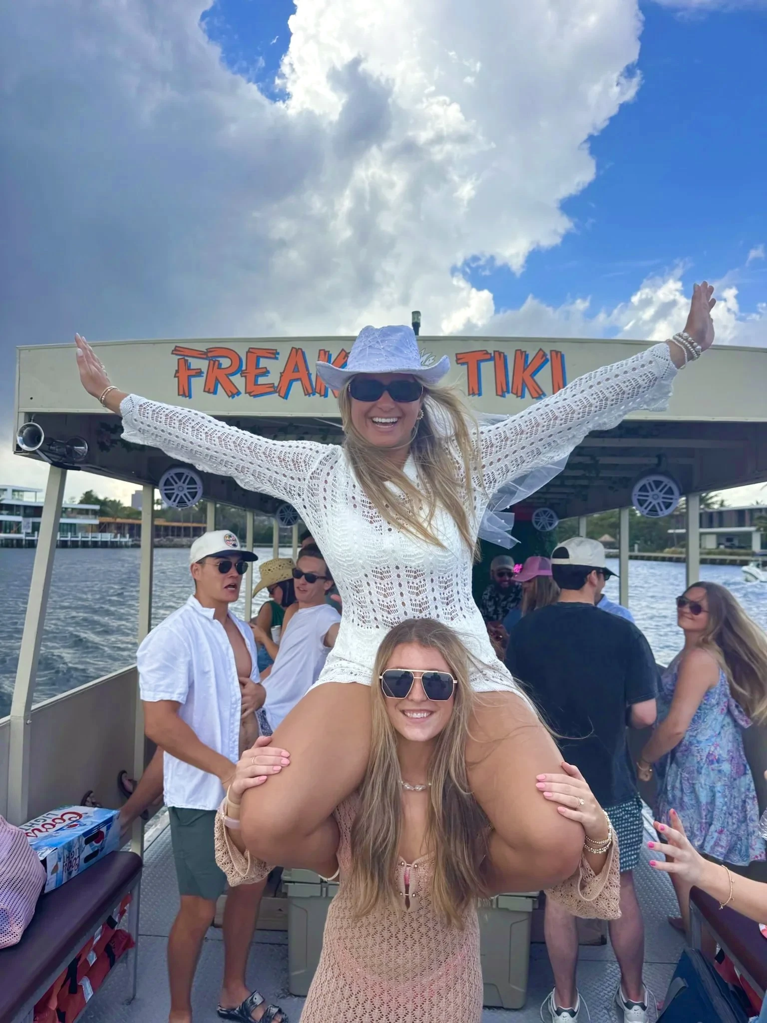 Bride in a white cowboy hat and cover-up riding on a friend's shoulders aboard Freaky Tiki in Fort Lauderdale