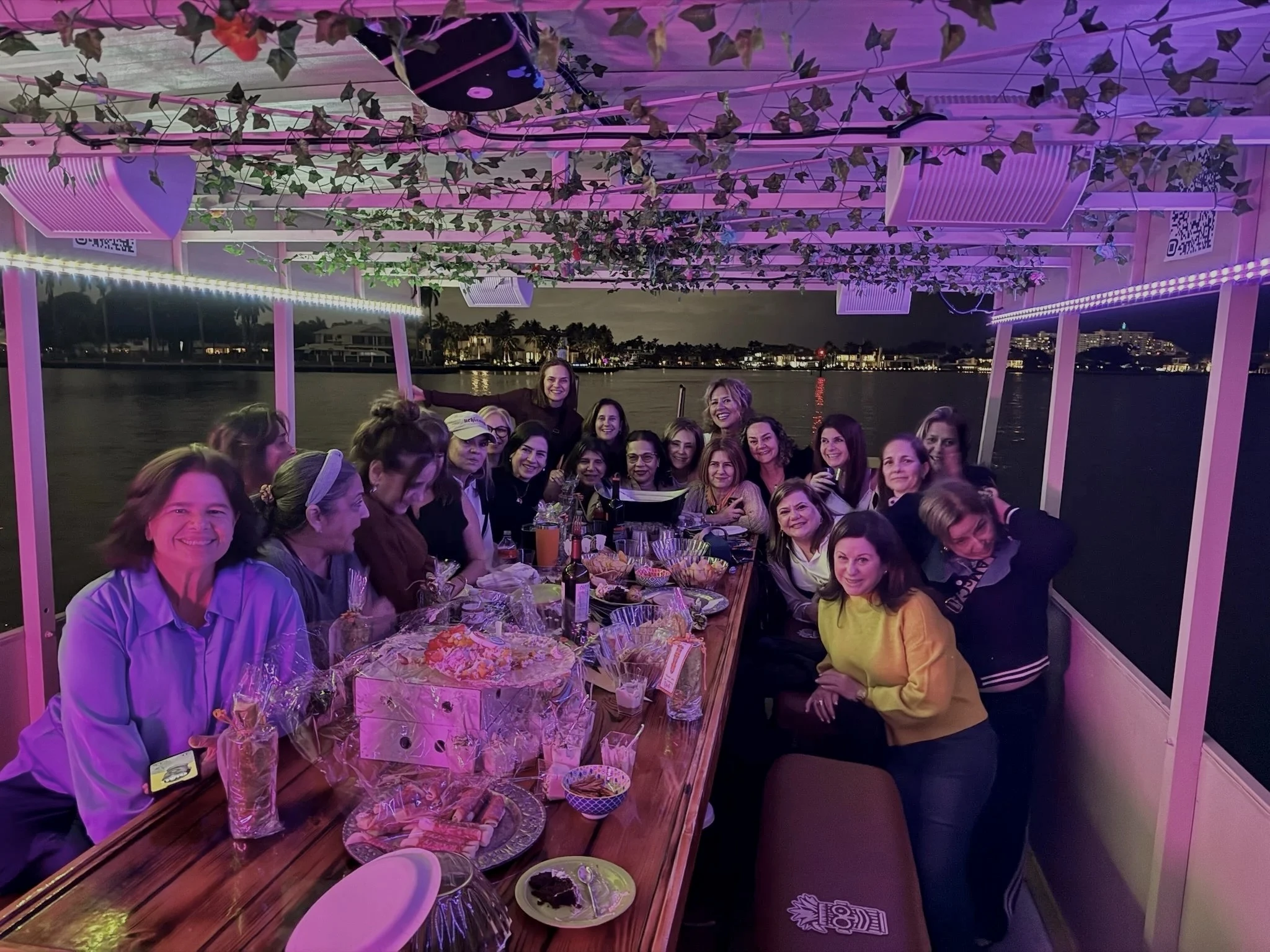 Women sharing an evening celebration around the Freaky Tiki table under purple deck lights in Fort Lauderdale