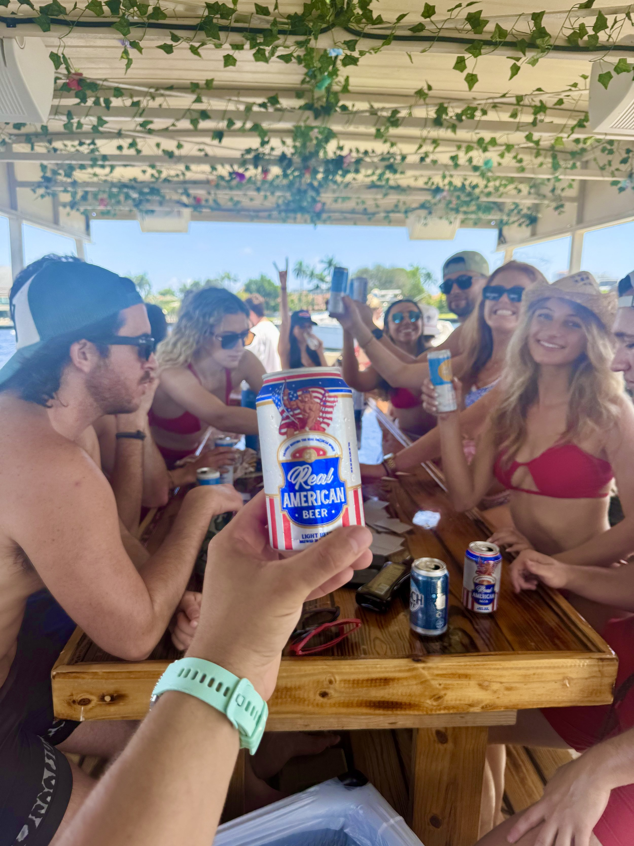 Adult group of friends raising drinks around the wooden Freaky Tiki table during a sunny Fort Lauderdale charter