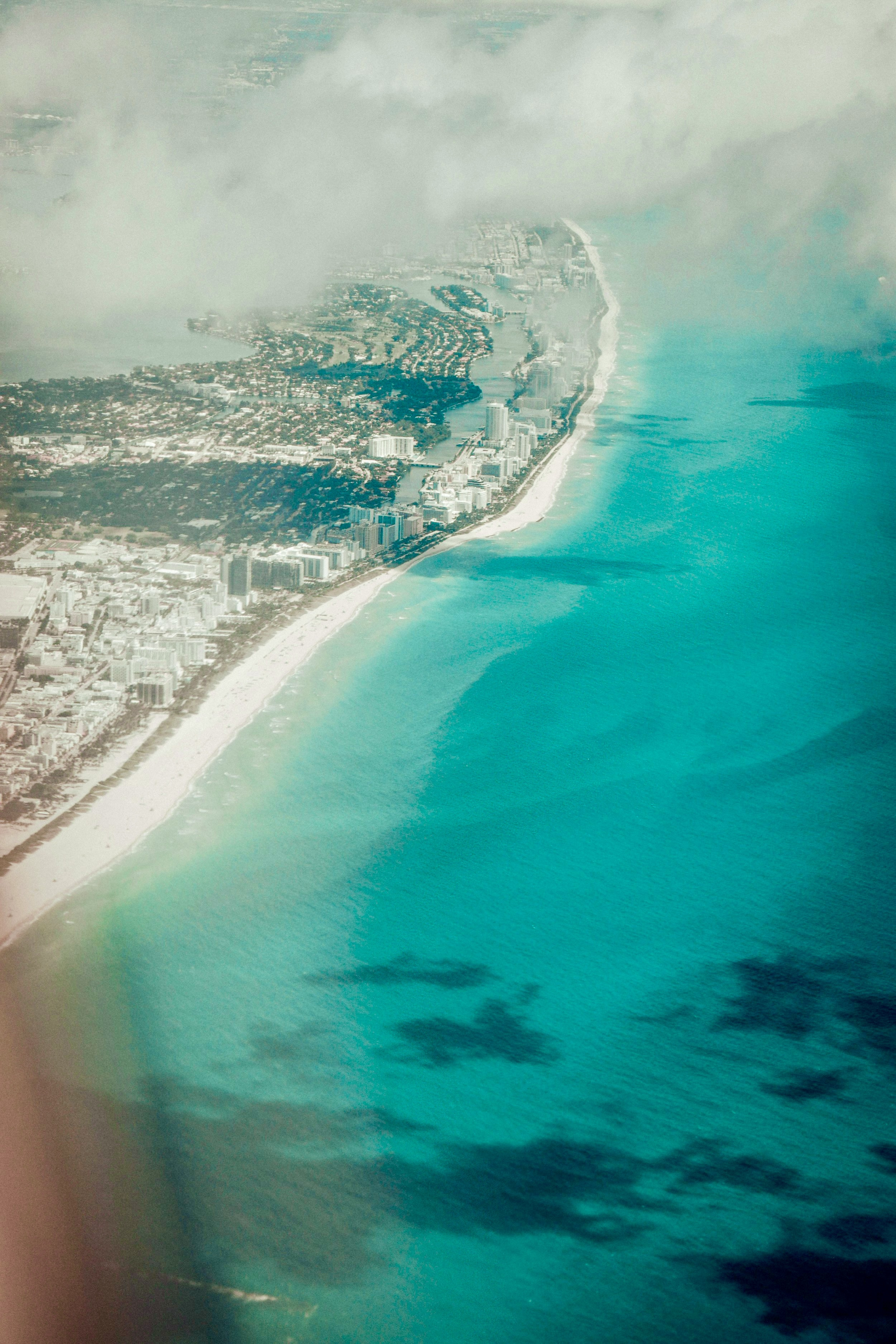 Aerial view of a South Florida coastline with beachfront buildings, clouds and turquoise ocean water